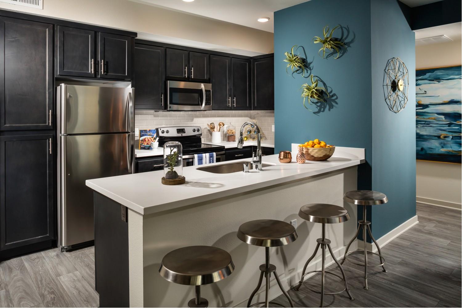 Kitchen with dark cabinets, stainless steel appliances and some tall stools