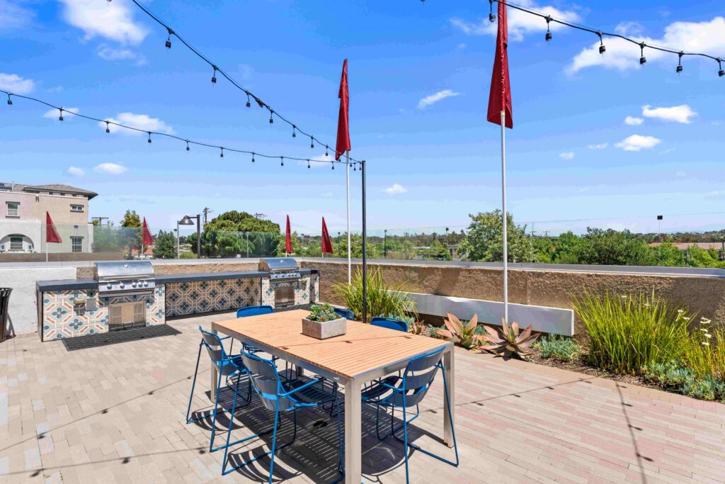 Outdoor patio with a wooden table, blue chairs, string lights and built-in grills.
