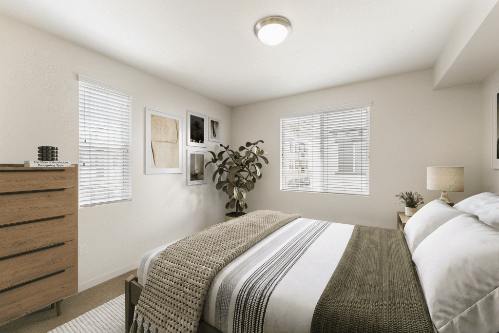 A modern bedroom featuring a bed with a textured knit throw, a wooden dresser, a potted plant, and framed wall art.