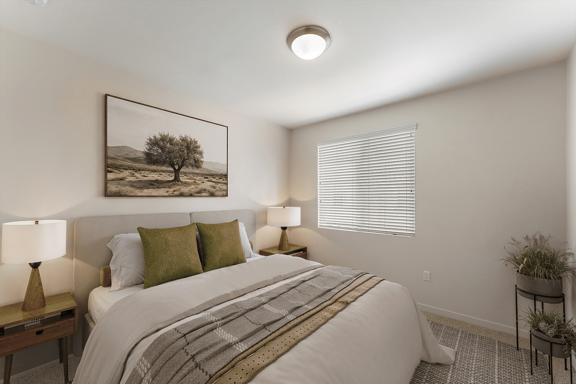 Bedroom with a bed, two nightstands with lamps, a framed landscape print on the wall, a window with blinds, and two potted plants on a metal stand.