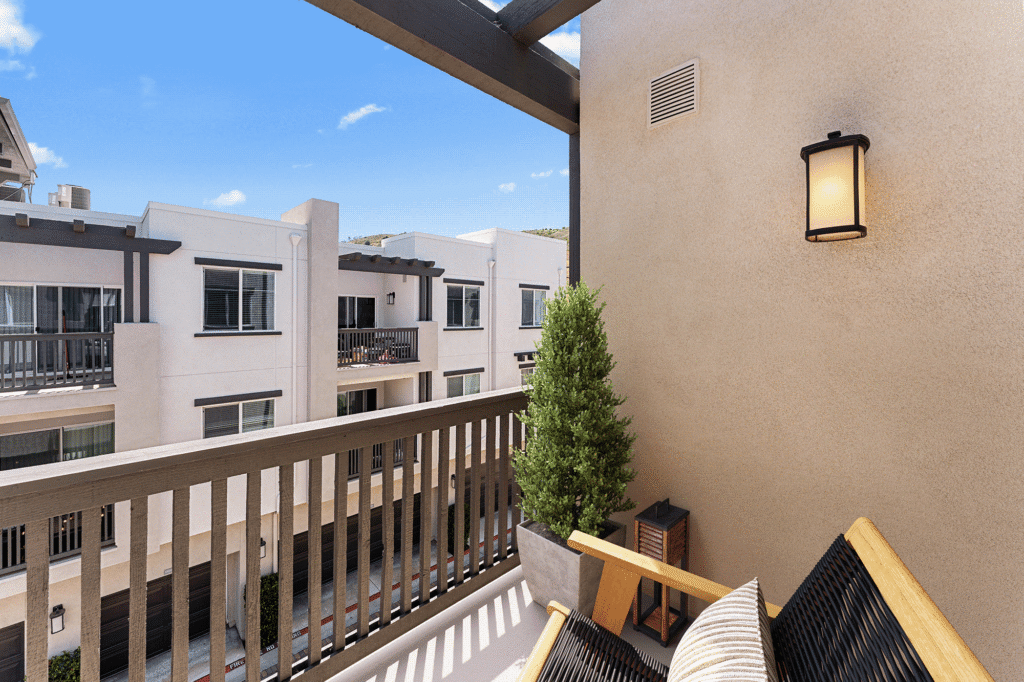 A small apartment balcony with a chair, a potted plant, and a view of a neighboring residential building.