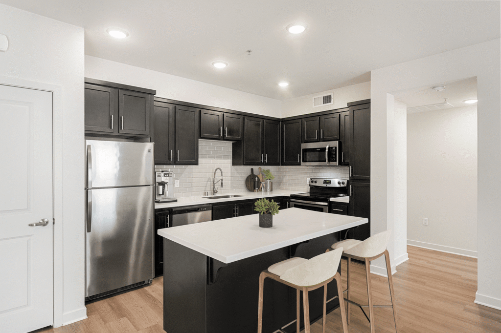 Kitchen with dark cabinets, white countertops, stainless steel appliances, and a central island with two stools.