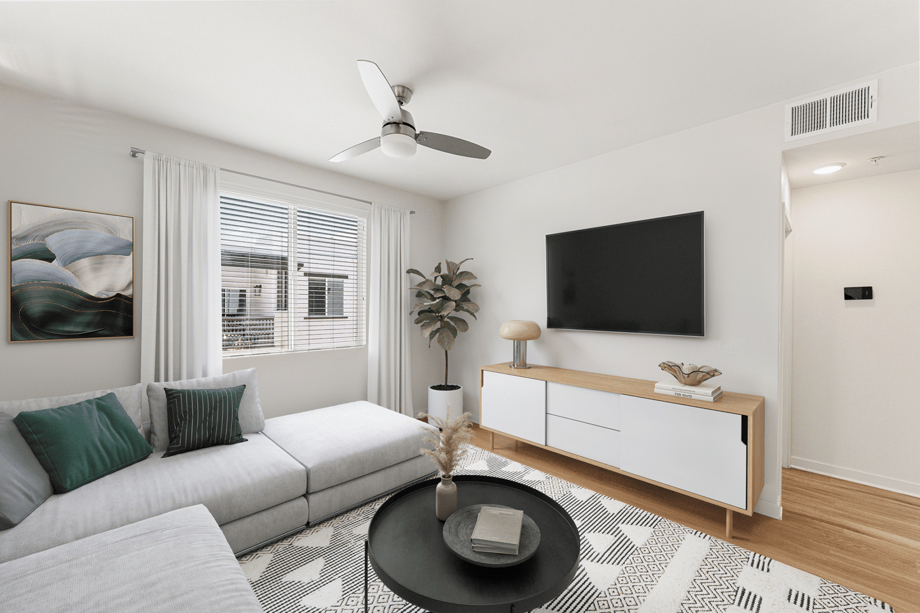 Living room featuring a light gray sectional sofa, a round coffee table, and a wall-mounted television above a white and wood media console.