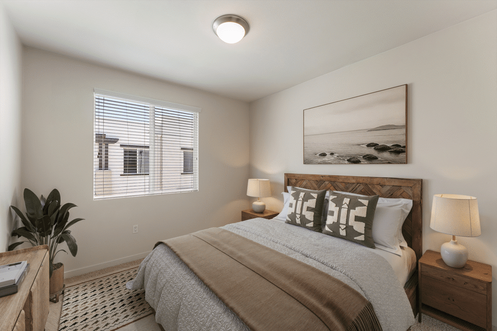 A bedroom with a wooden bed frame, patterned throw pillows, and two bedside lamps under a ceiling light.